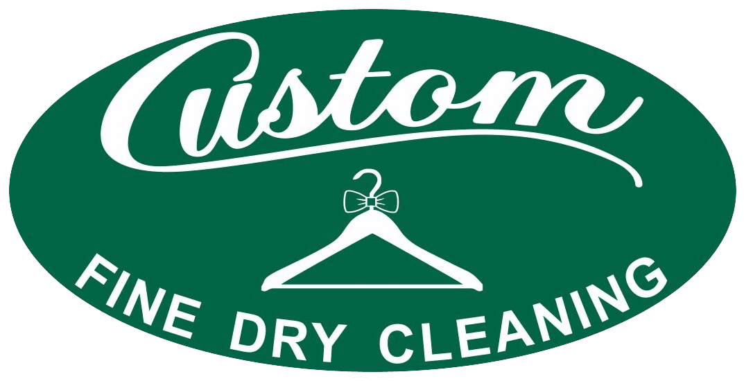 A green oval sign with "Custom" in script, a hanger with a bowtie, and "FINE DRY CLEANING" in bold white letters.