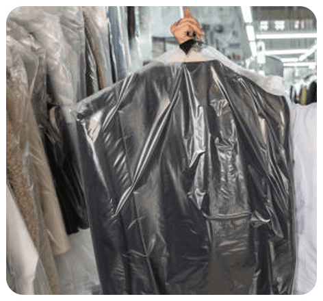 A person holds up a suit covered in a plastic garment bag inside a dry cleaning shop.
