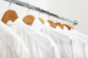 Several white dress shirts hang neatly on wooden hangers along a metal clothing rack against a light background.