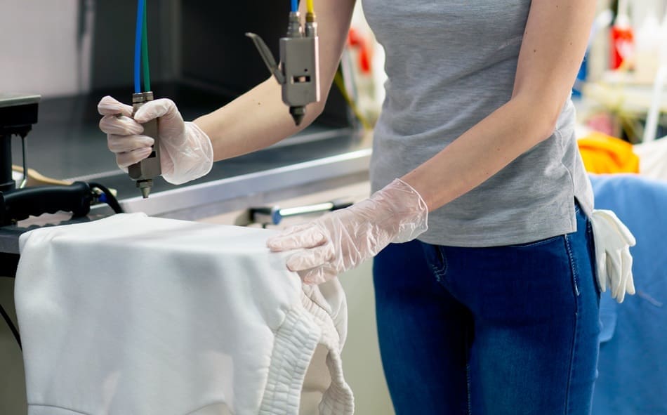 Person wearing gloves uses specialized equipment to clean a white garment, suggesting a professional cleaning or stain removal process.